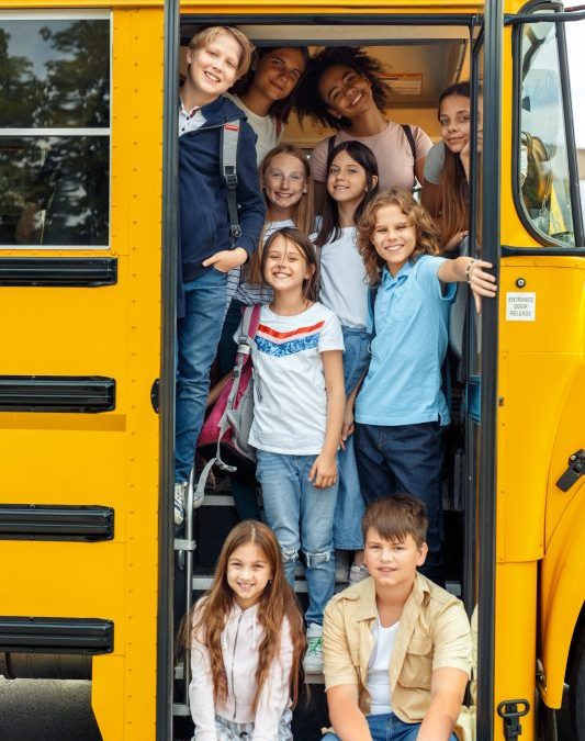 10 children on the bus standing at the door of the bus all smiling
