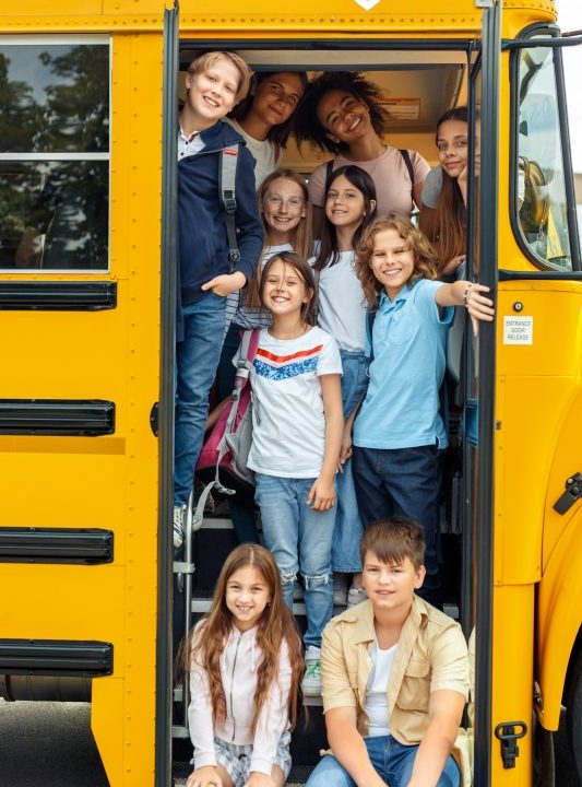 10 children on the bus standing at the door of the bus all smiling