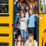 10 children on the bus standing at the door of the bus all smiling