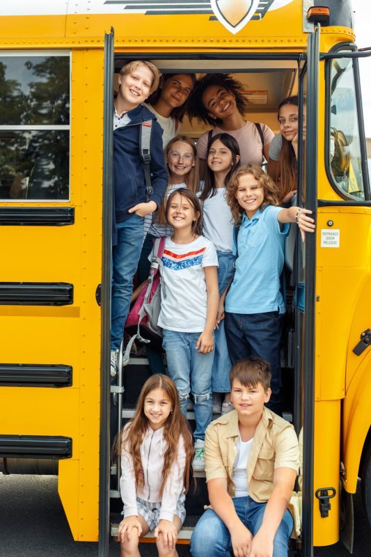10 children on the bus standing at the door of the bus all smiling