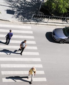 Three people in an intersection with a car waiting for them to pass