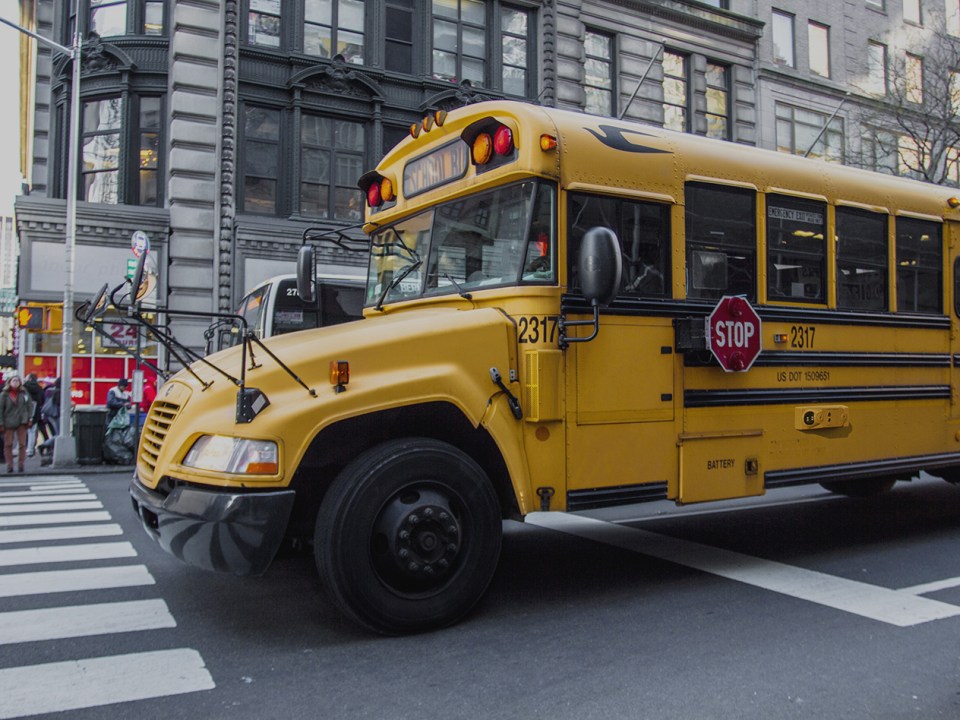 Yellow school bus stopped at intersection on a busy city street.