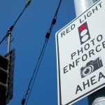 Low angle view of a red light photo enforcement sign and traffic light at an intersection.