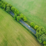 Aerial view of car driving on a road under trees in a green landscape