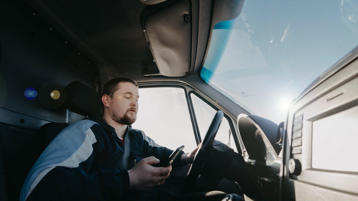 male truck driver with a smartphone in his hands is driving