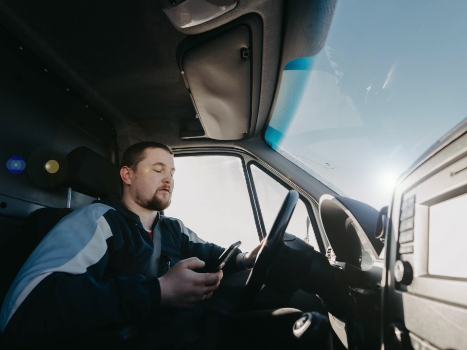 male truck driver with a smartphone in his hands is driving