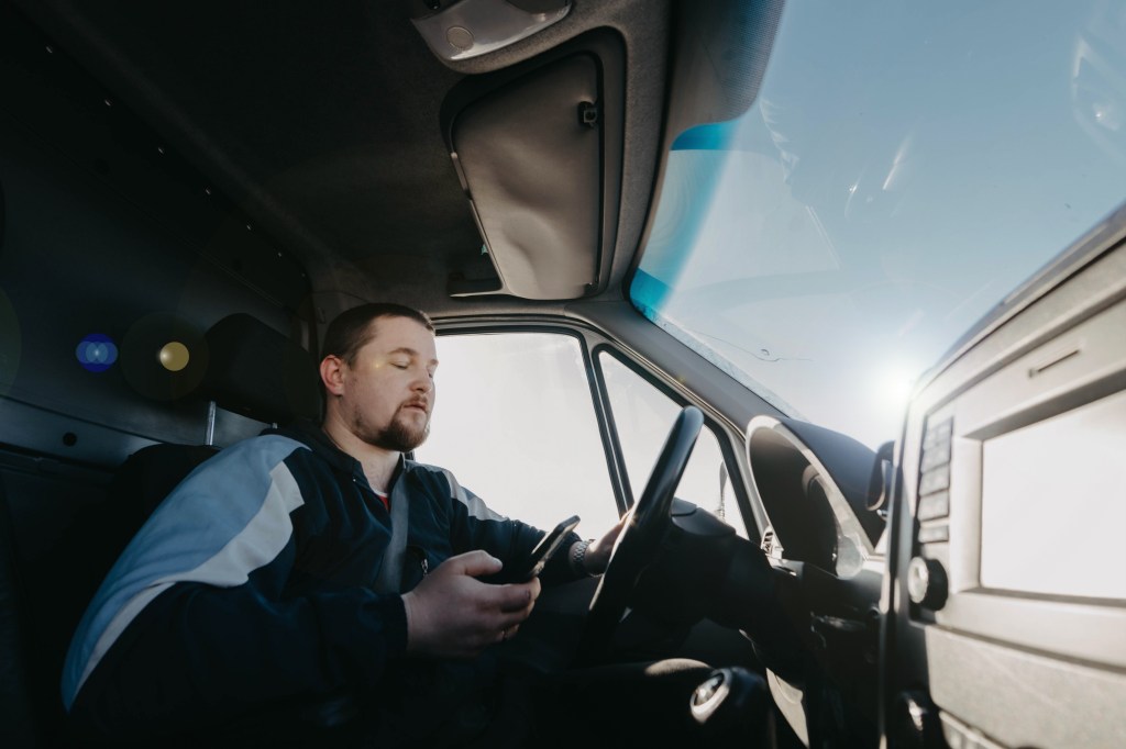 male truck driver with a smartphone in his hands is driving