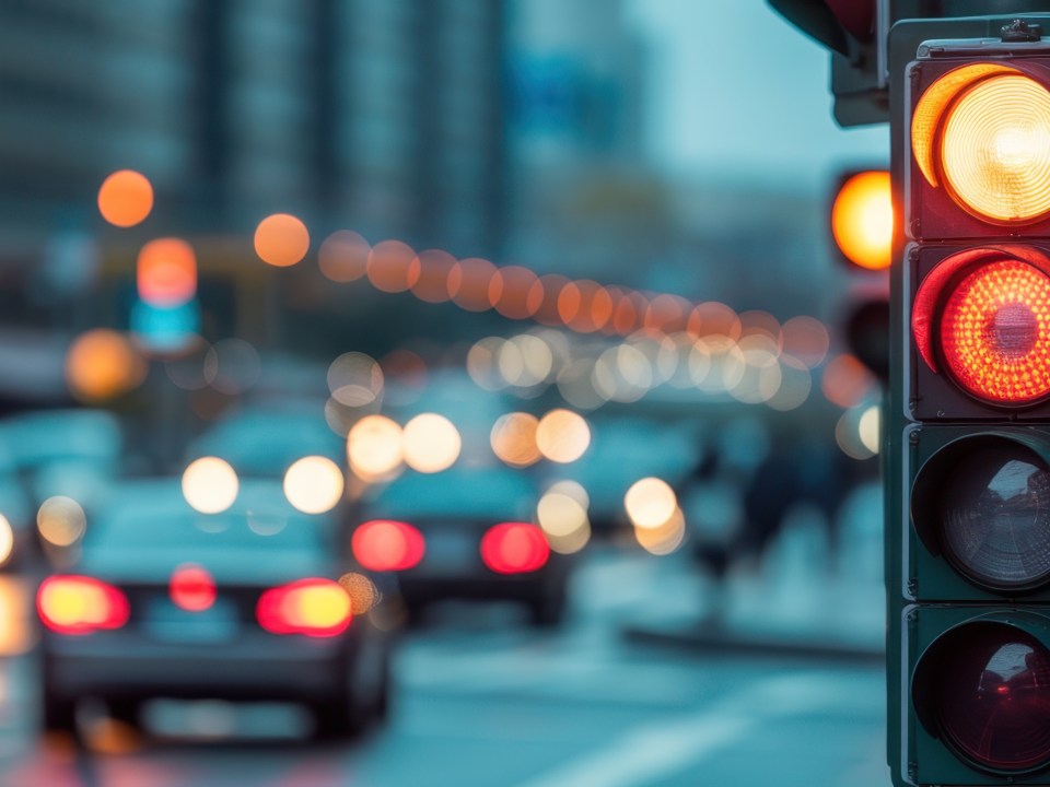 A traffic light at a street crossroads with a beautiful bokeh city and cars in the background.