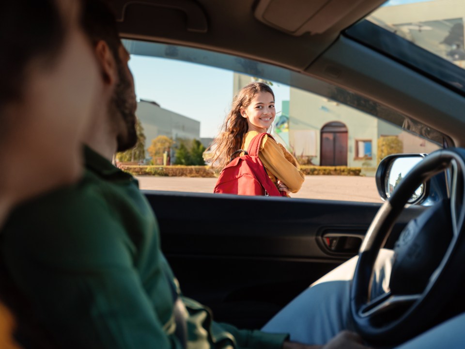 Mother and father dropping off daughter in front of school, schoolgirl turning back to parents sitting in car and smiling, view from inside auto