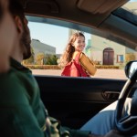 Mother and father dropping off daughter in front of school, schoolgirl turning back to parents sitting in car and smiling, view from inside auto