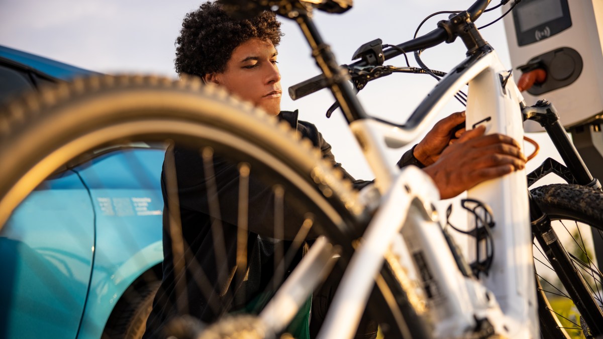 Young man inserting plug into electric bicycle for charging at electric charging station