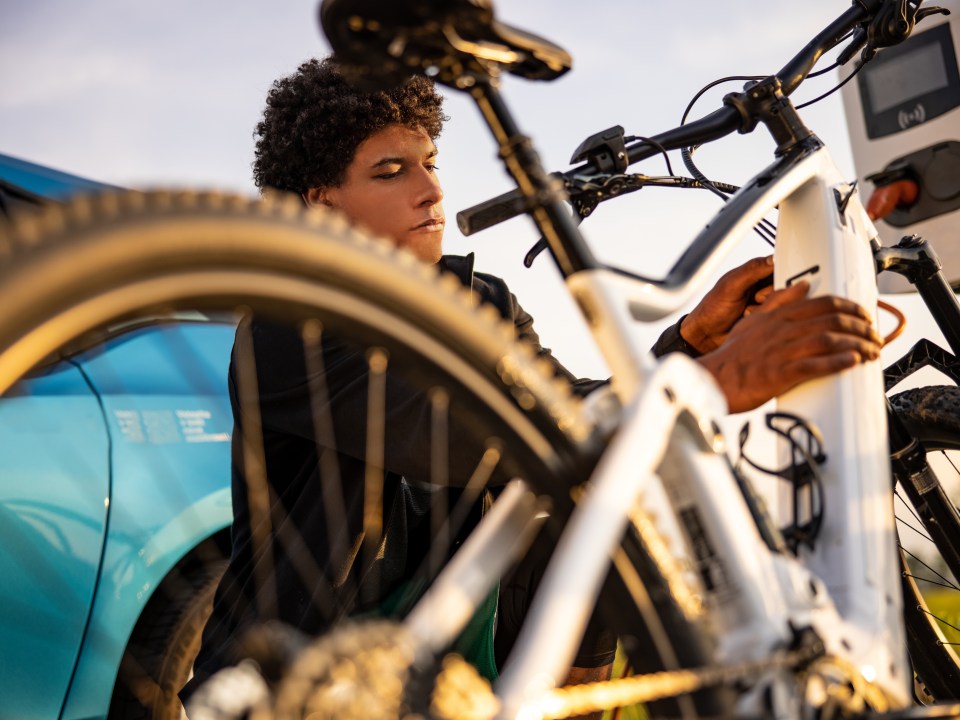 Young man inserting plug into electric bicycle for charging at electric charging station
