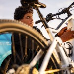 Young man inserting plug into electric bicycle for charging at electric charging station