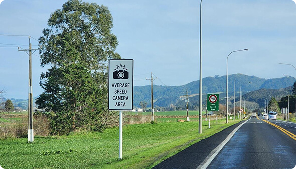long stretch of road with custom white and black sign "average speed camera area"
